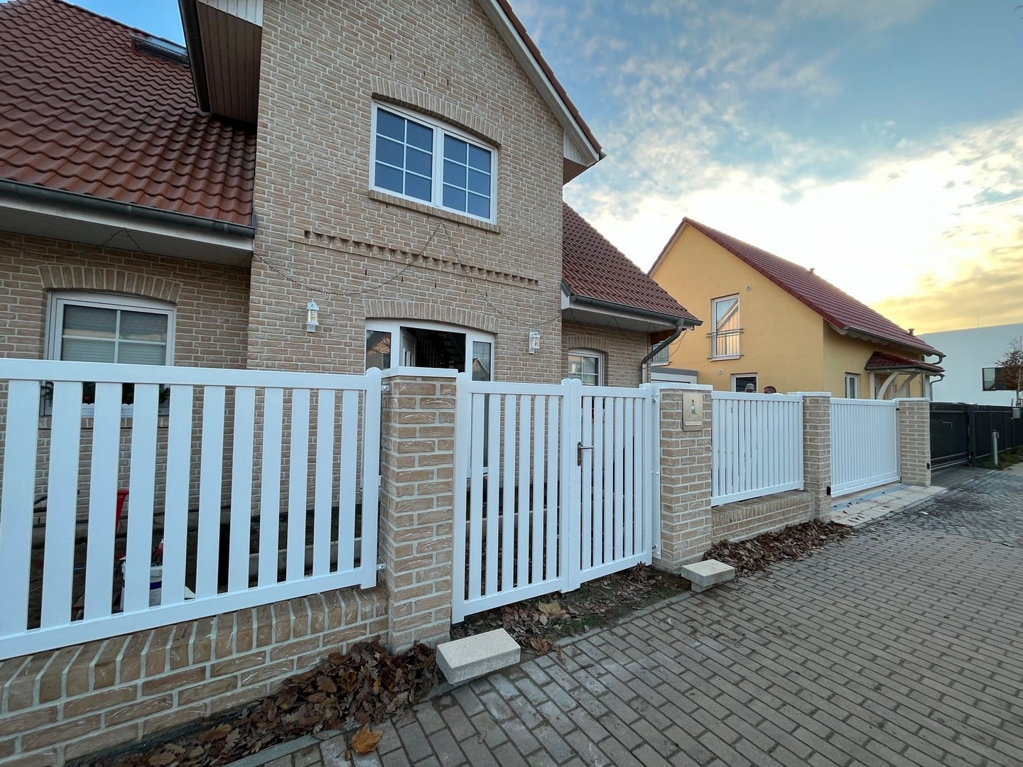 Einfamilienhaus mit Ziegelsteinfassade und weißem Zaun.