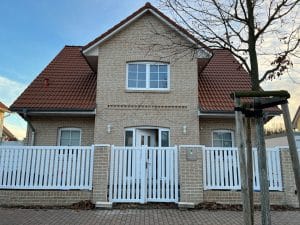 Zweistöckiges Haus mit Ziegeldach und weißem Zaun