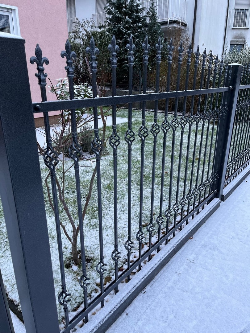 Schmiedeeiserner Zaun mit leichtem Schneefall.