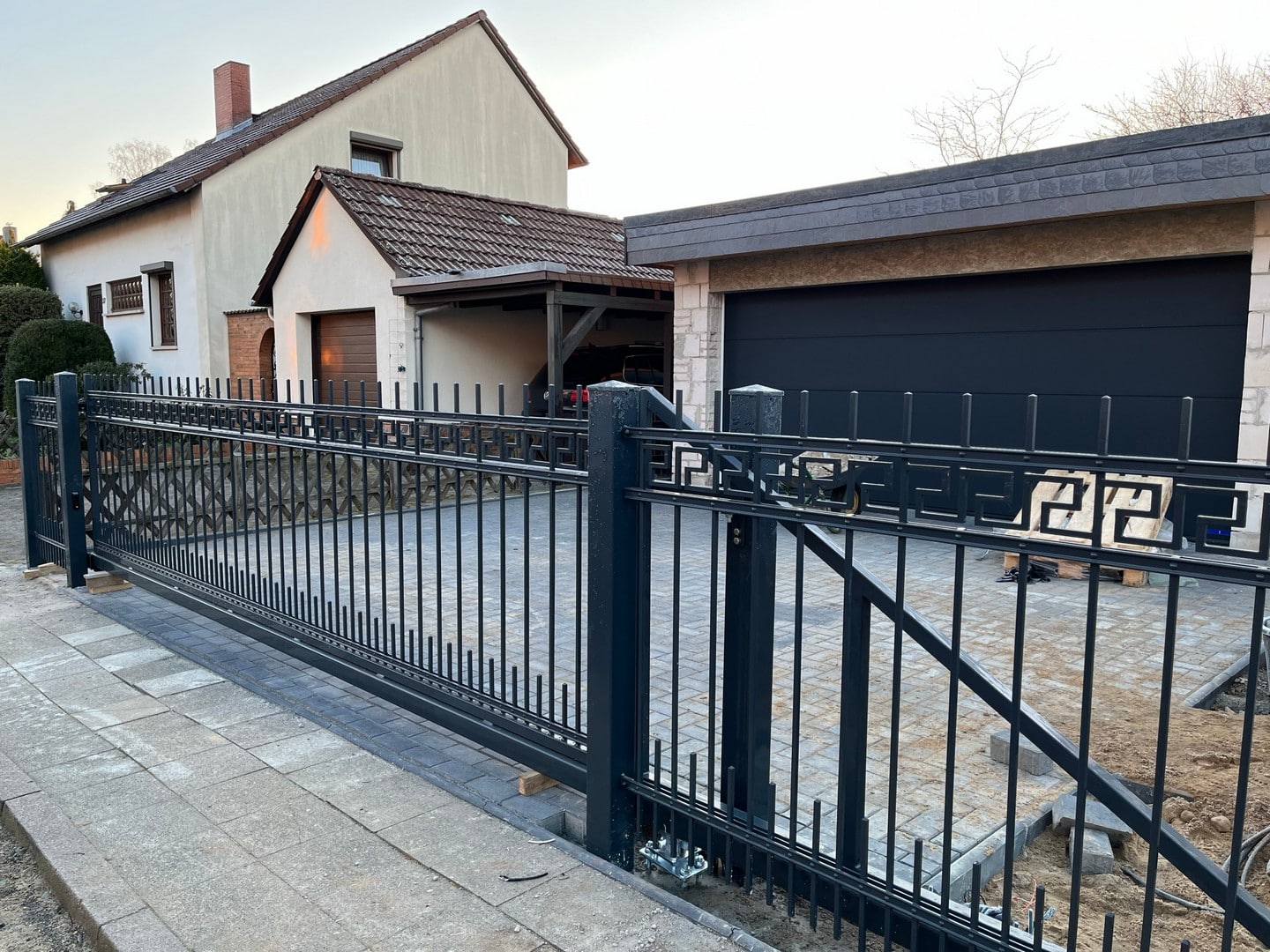 Einfamilienhaus mit Einfahrtstor und Garage bei Dämmerung.