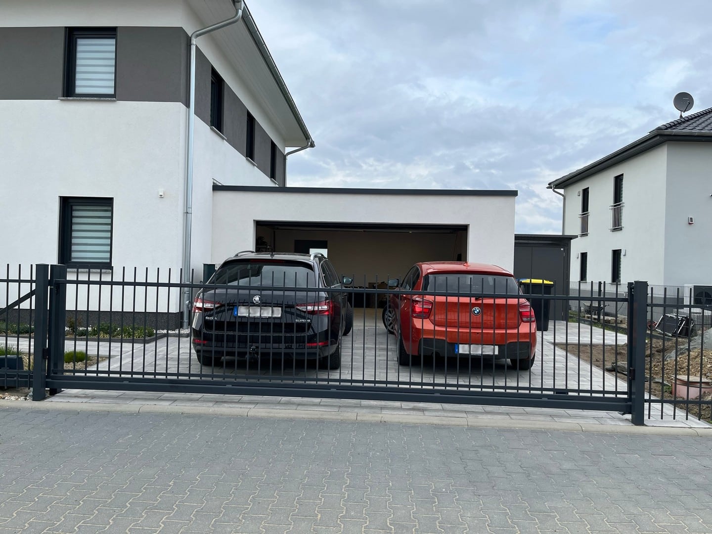 Zwei Autos vor modernem Einfamilienhaus mit Carport.