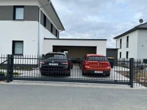 Zwei Autos vor modernem Einfamilienhaus mit Carport.