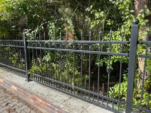 Schmiedeeiserner Zaun vor grünen Sträuchern.