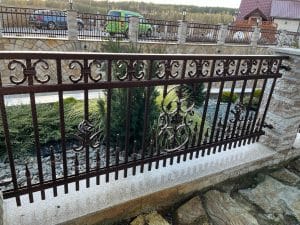 Schmiedeeisernes Geländer mit Verzierungen und Landschaft im Hintergrund.
