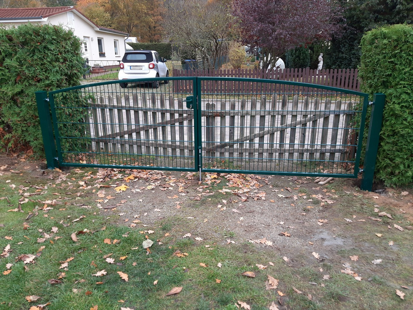 Grünes Gartentor mit Einfahrt und Herbstlaub.