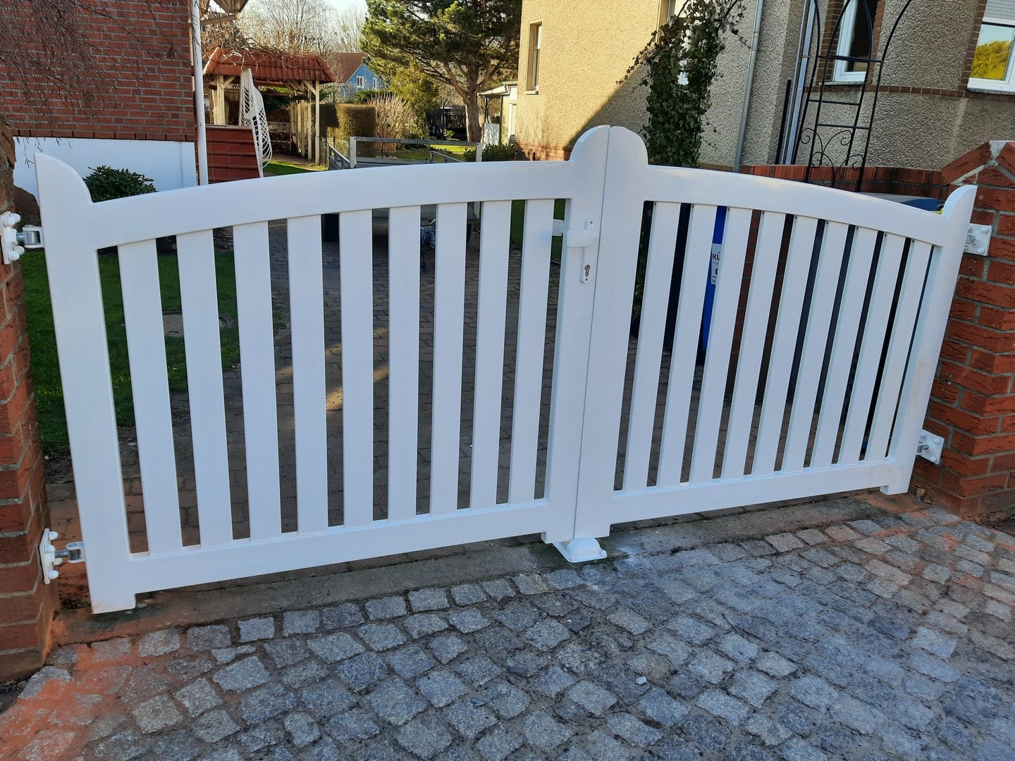 Weißes Gartentor aus Holz auf Kopfsteinpflasterweg.