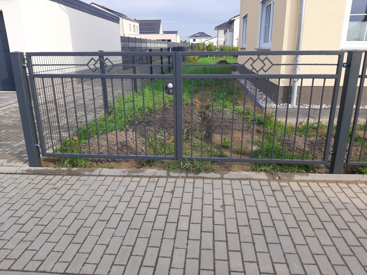 Metallgartentor mit Pflasterweg und Grasfläche.