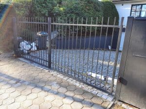 Metalltor Einfahrt mit Pflastersteinen und Mülltonnen.