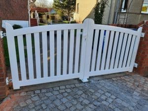 Weißes Gartentor aus Holz auf Kopfsteinpflasterweg.