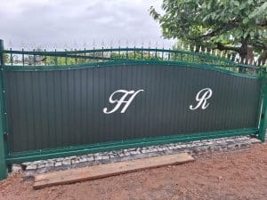 Elegantes grünes Schiebetor mit dekorativen Spitzen und individuellen Buchstaben, hergestellt von KOMABUD.