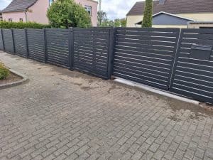 Moderner Metallzaun mit horizontalen Lamellen und integriertem Tor mit Briefkasten, hergestellt von KOMABUD.