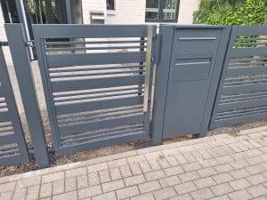 Modernes Metallzauntor mit integriertem Briefkasten und horizontalen Lamellen, hergestellt von KOMABUD.