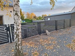 Moderner Metallzaun mit horizontalen Lamellen und Eingangspforte, hergestellt von KOMABUD.