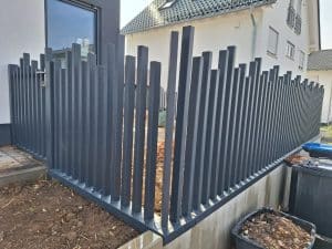 Moderner Metallzaun mit vertikal angeordneten Lamellen in unterschiedlicher Höhe, hergestellt von KOMABUD.